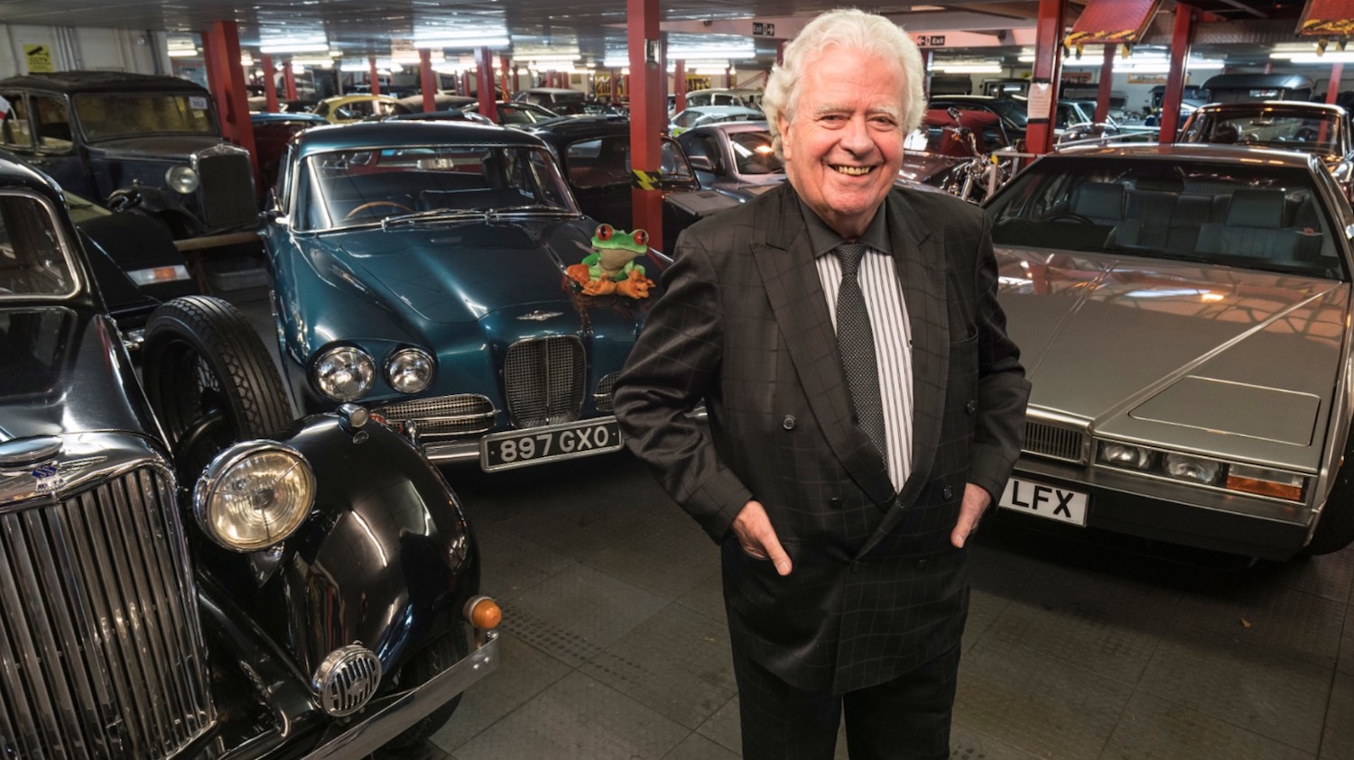 Rodger Dugging standing in his luxury car garage filled with rare classic and modern vehicles